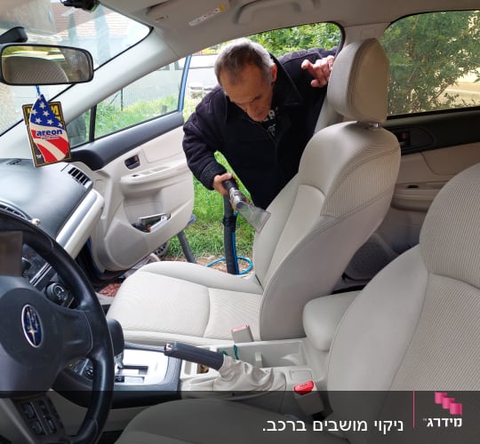 אדם מנקה מושב רכב עם שואב אבק